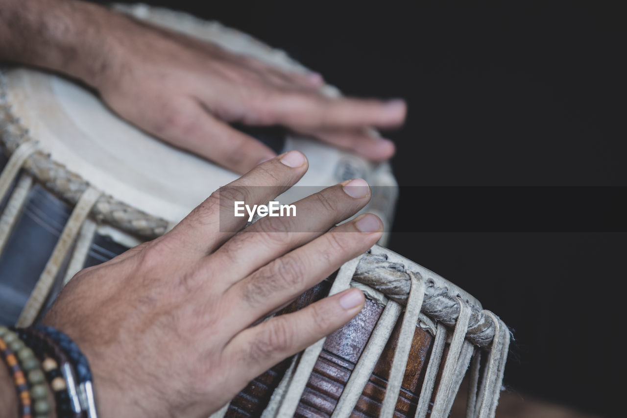 Cropped hands of man playing tabla against black background