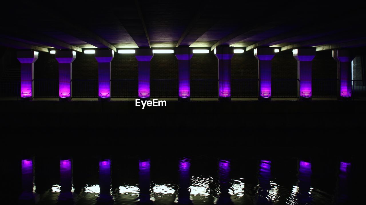 Reflection of purple illuminated columns in river at night