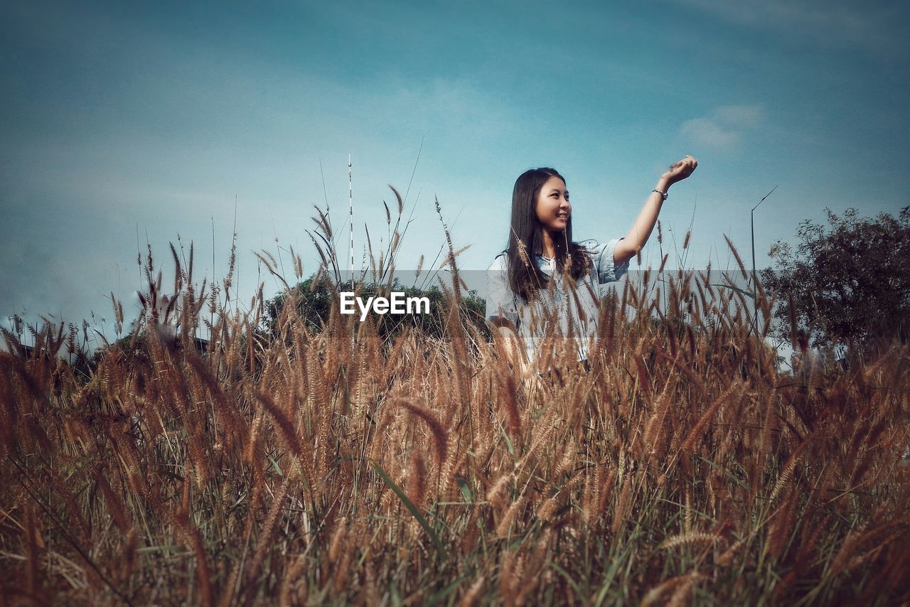 Low angle view of girl holding reed while standing on field against sky