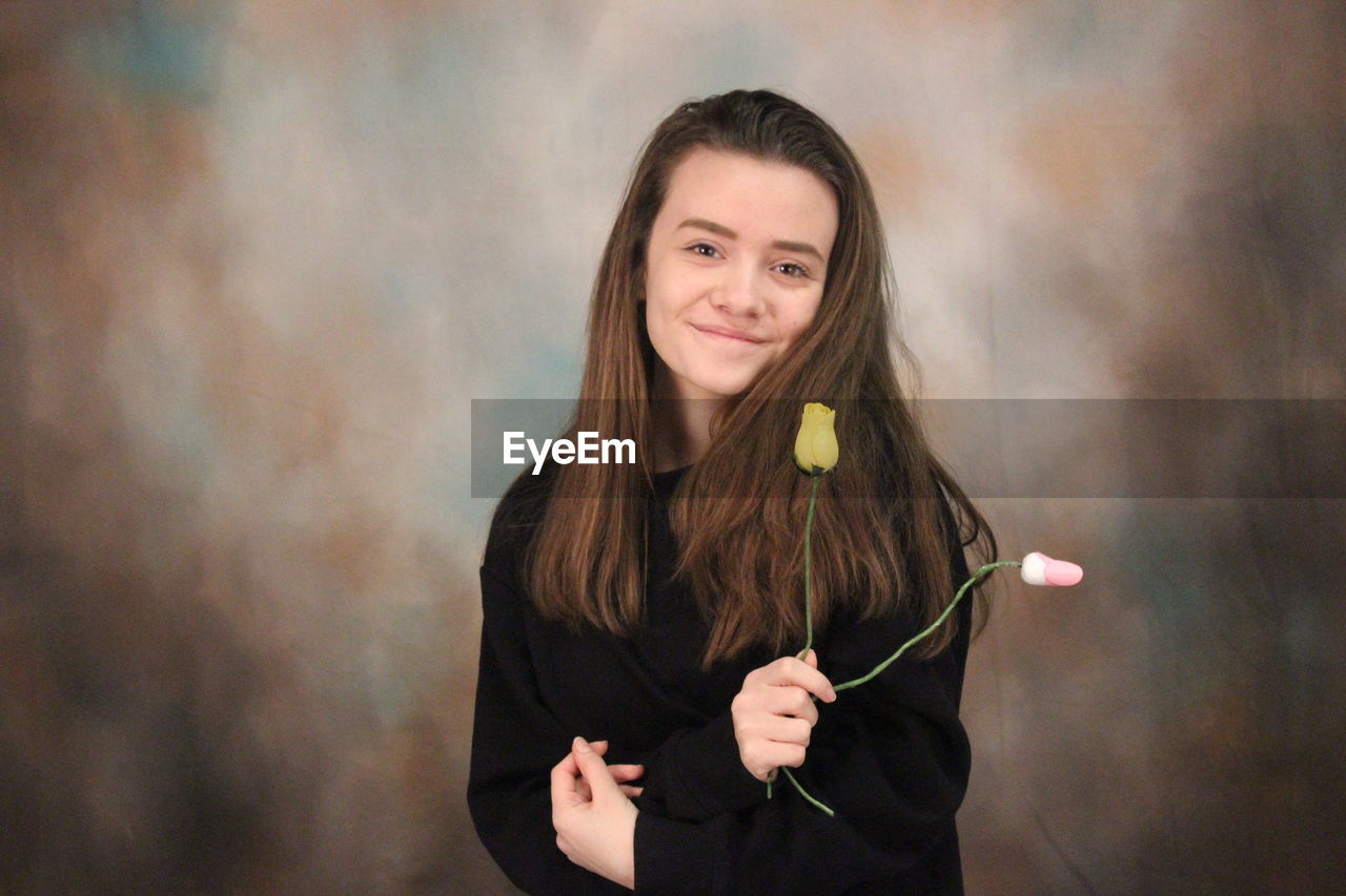 Portrait of smiling woman holding roses while standing against backdrop