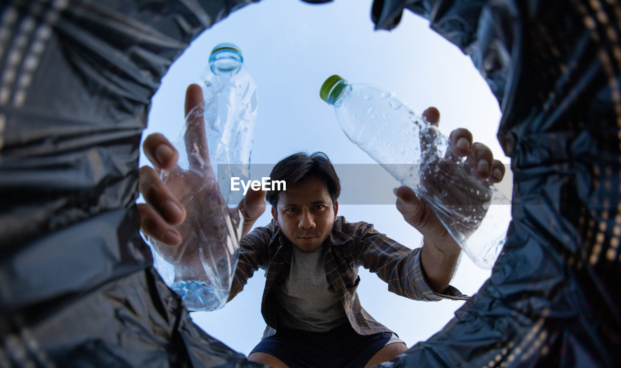 Portrait of man putting bottles in garbage can