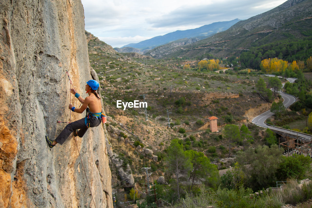 Shirtless man rock climbing against landscape