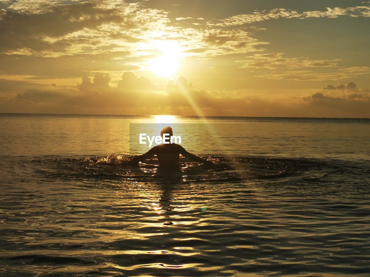 SILHOUETTE BOY ON SEA AGAINST SKY DURING SUNSET