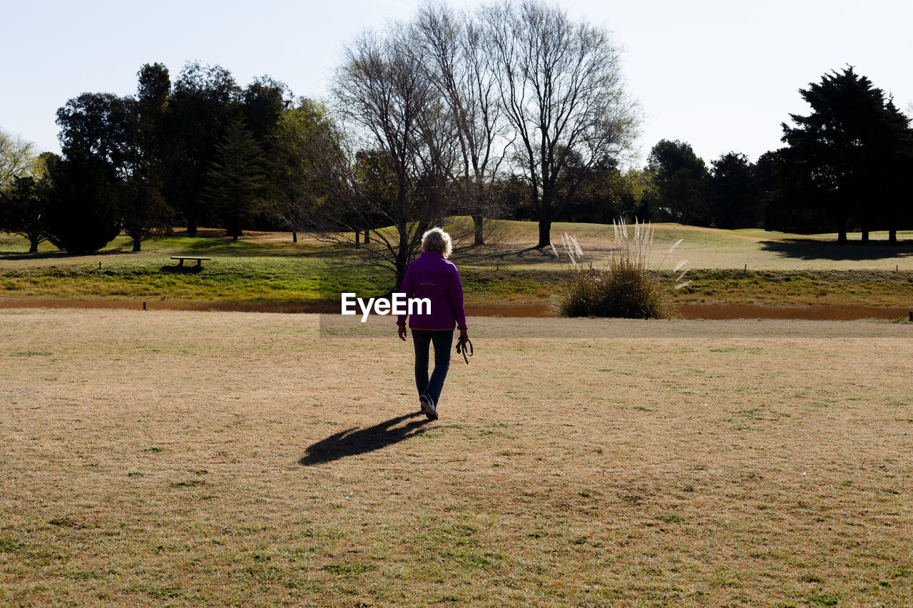 REAR VIEW OF WOMAN WALKING ON FIELD