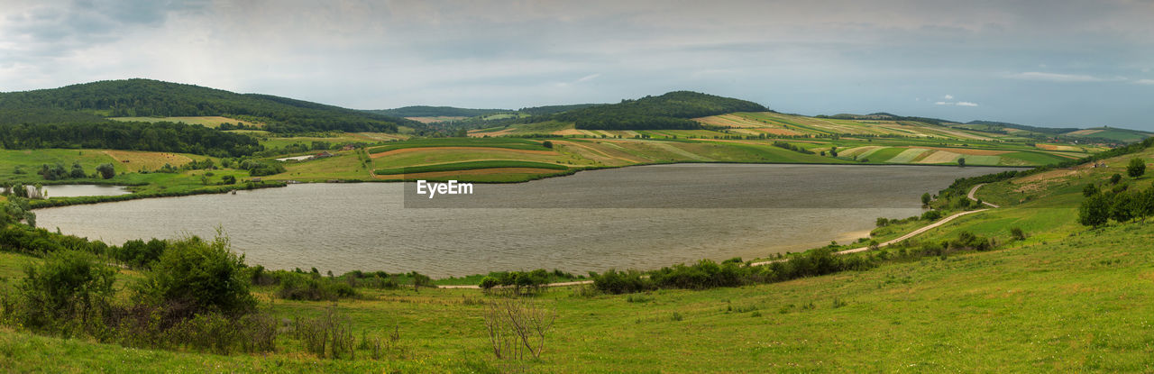Scenic view of green landscape and river against sky