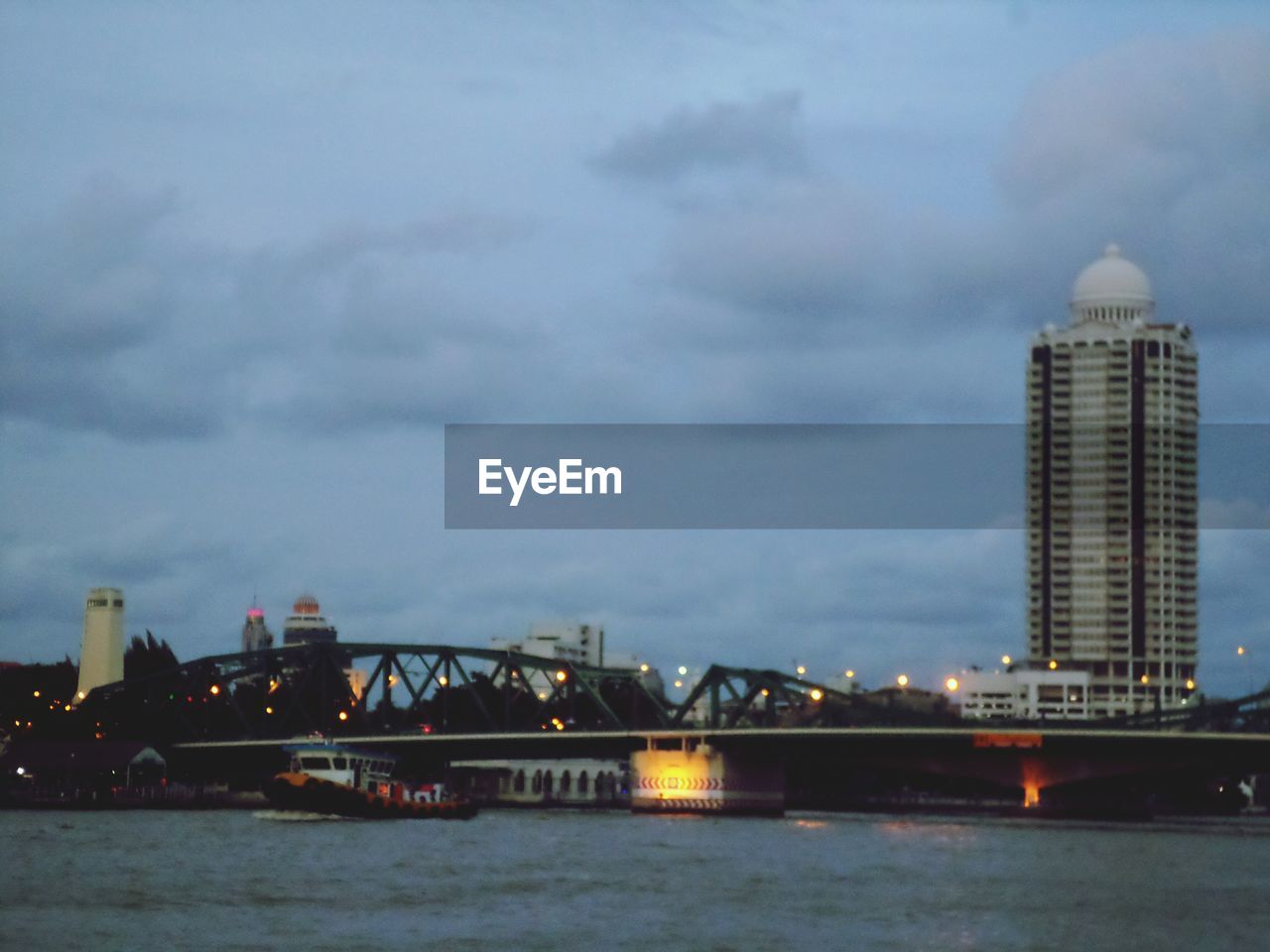 ILLUMINATED BRIDGE OVER RIVER BY CITY BUILDINGS AGAINST SKY