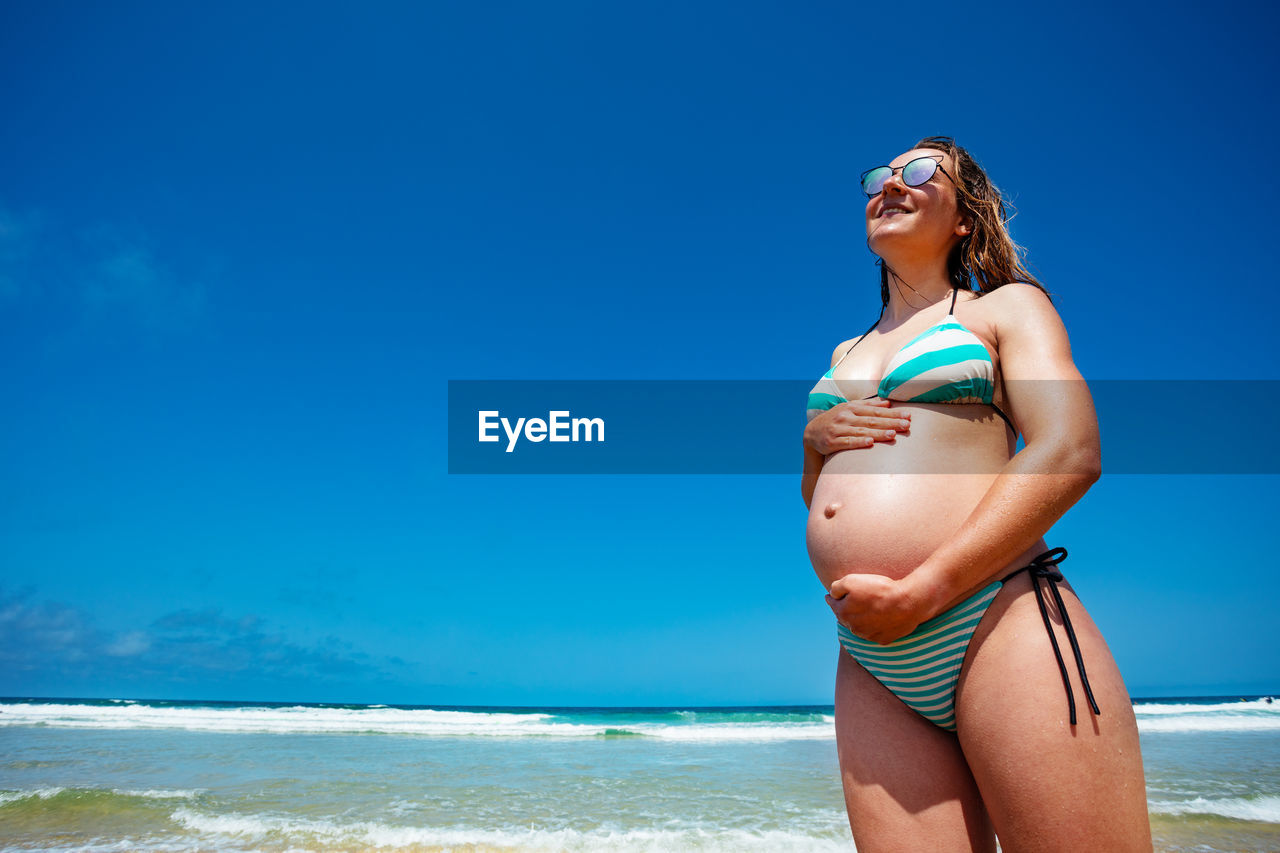 portrait of young woman in bikini standing at beach