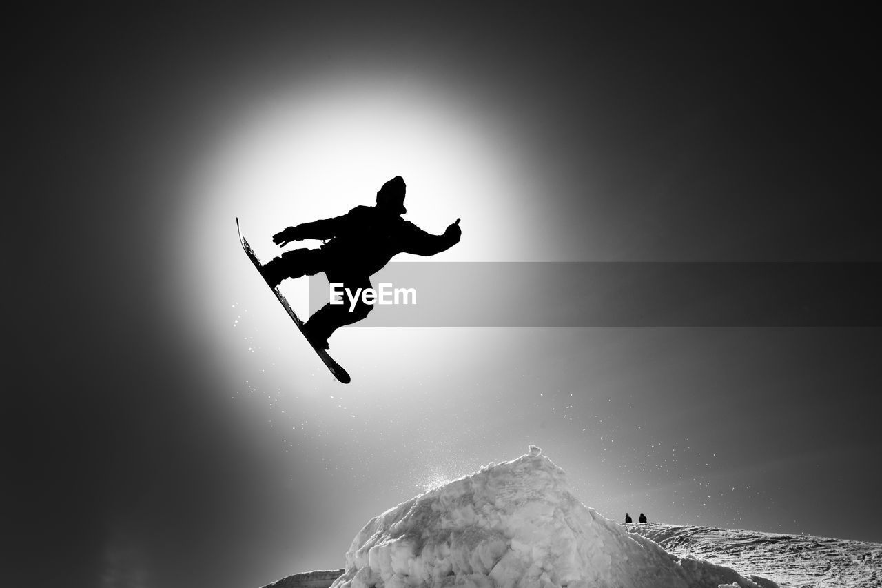 Silhouette person jumping on rock against sky