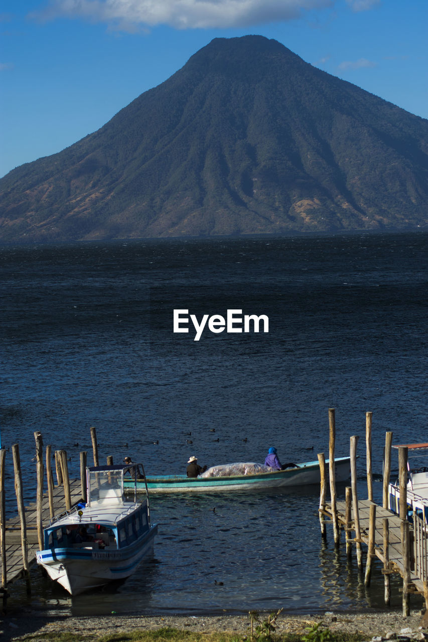 BOATS MOORED IN SEA AGAINST MOUNTAINS