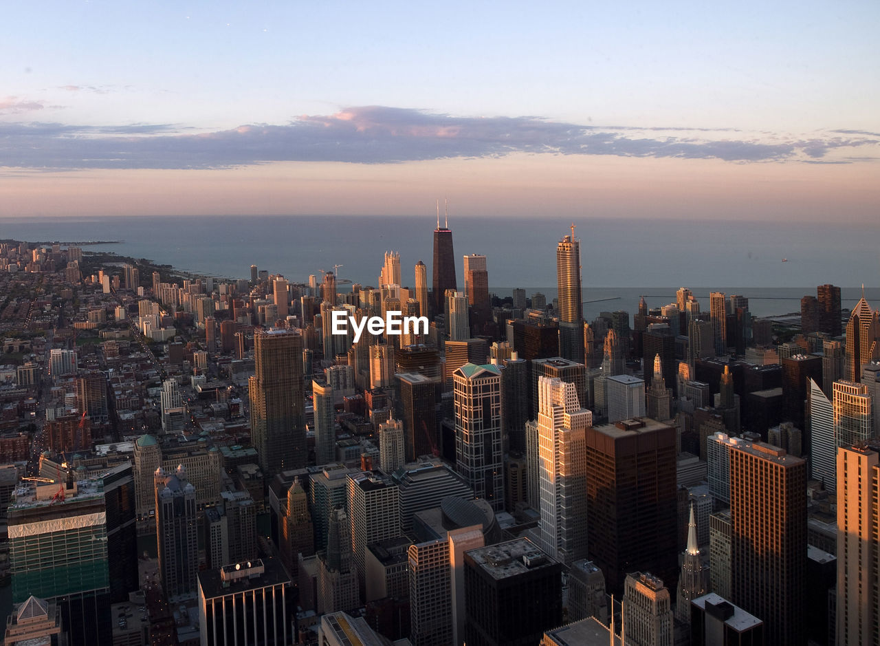 High angle view of cityscape by sea against sky during sunset