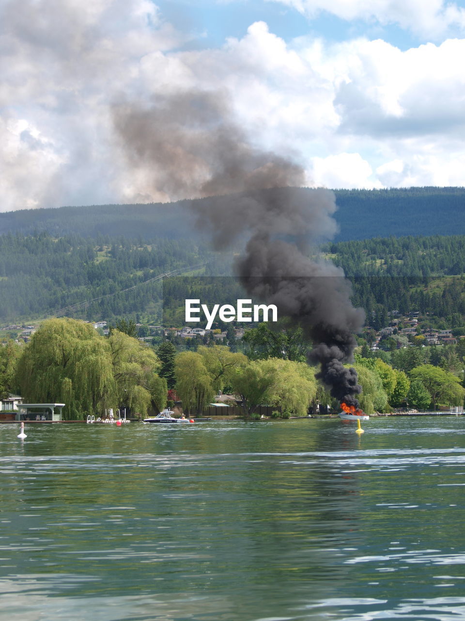 Distant view of burning boat in lake against sky