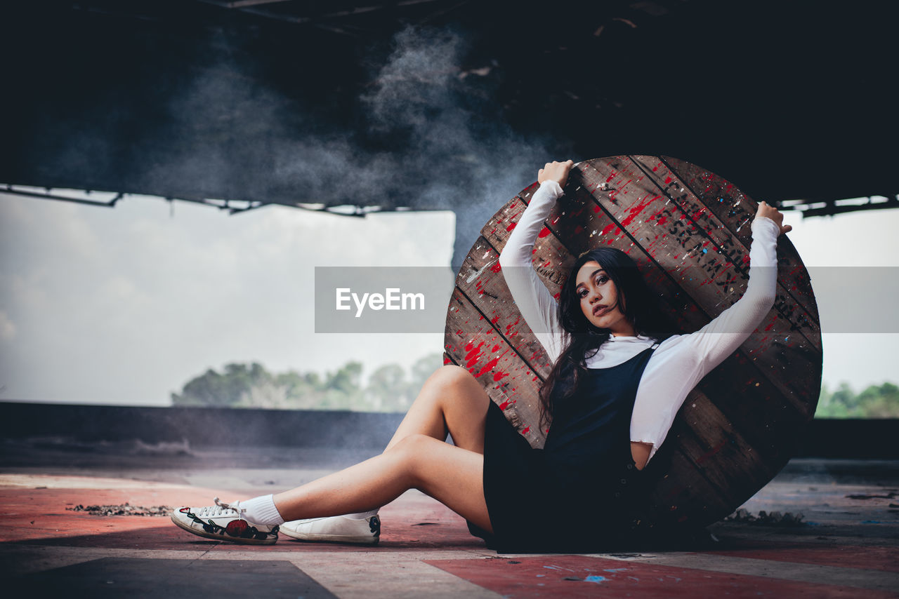 Portrait of young woman leaning on wooden table while sitting on floor