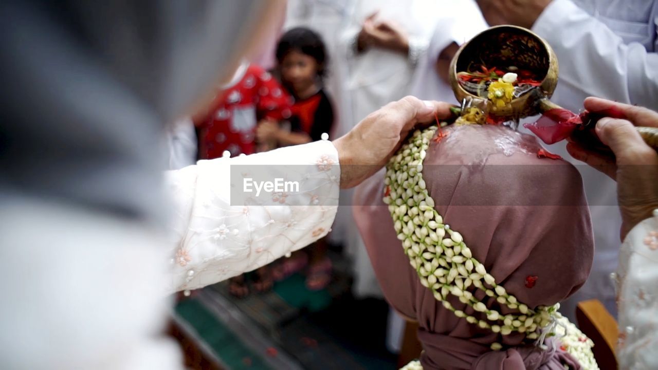 Cropped hands of woman pouring liquid on bride head