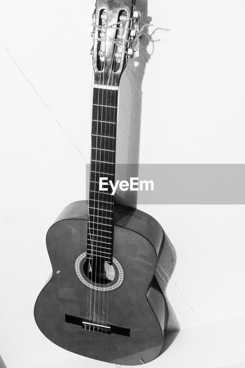 CLOSE-UP OF GUITAR AGAINST WALL AGAINST WHITE BACKGROUND