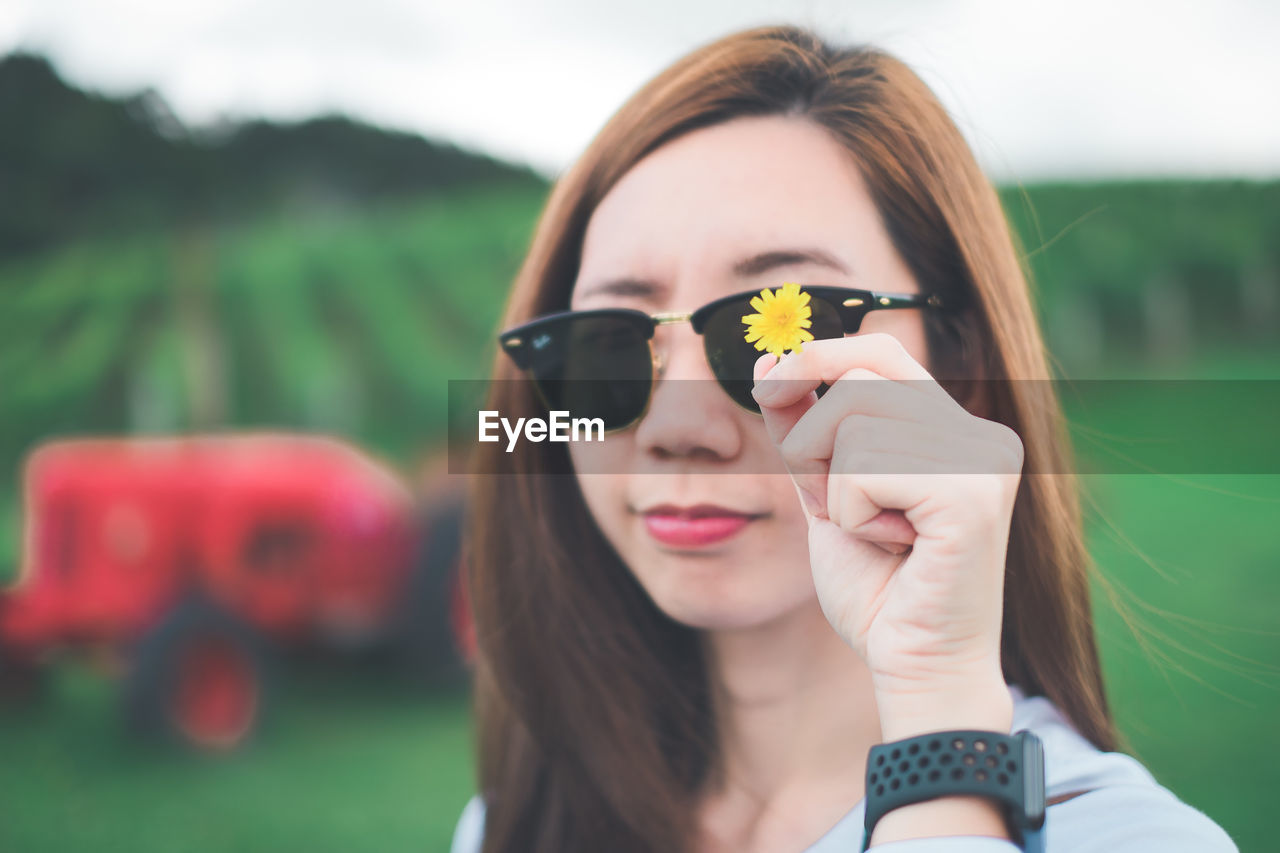 Close-up portrait of young woman in sunglasses holding yellow flower