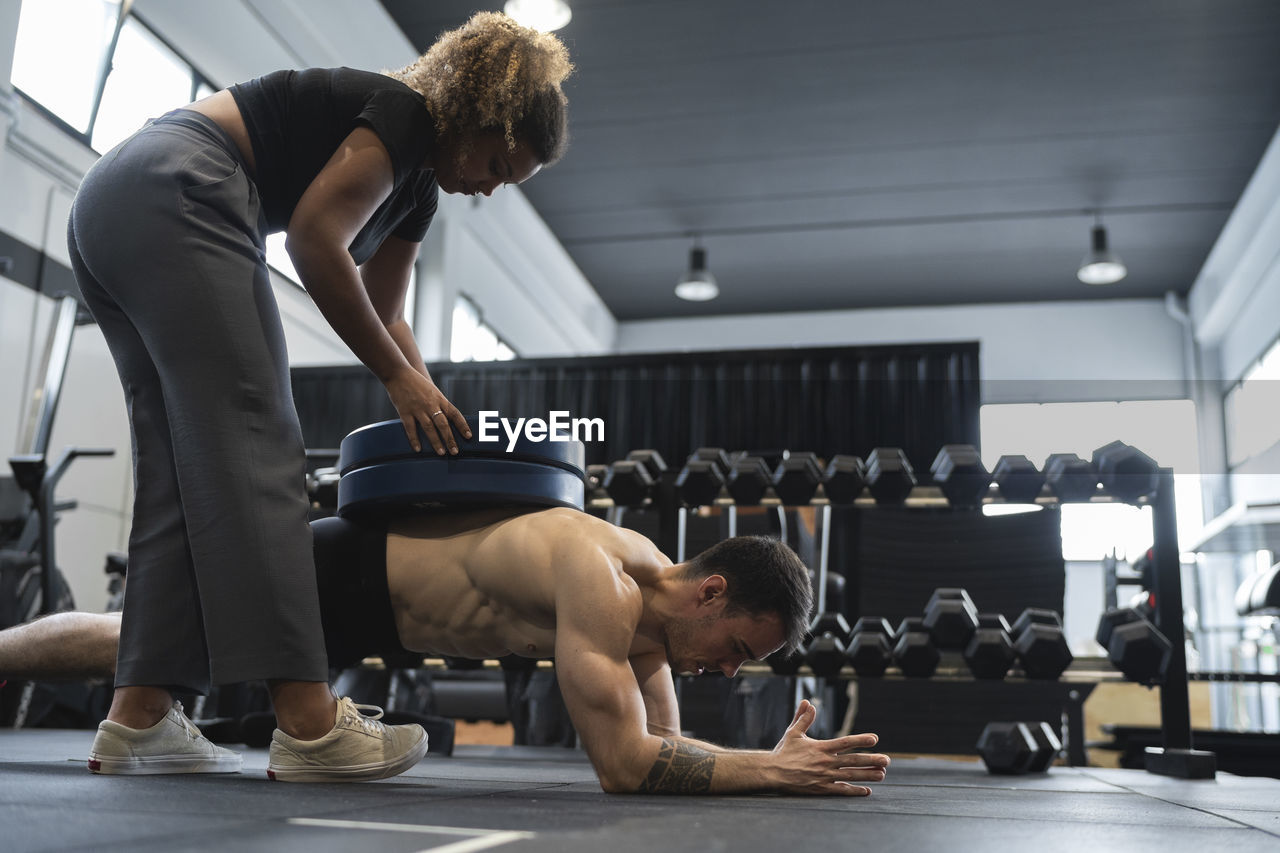 Fitness instructor training male athlete to do plank position in gym