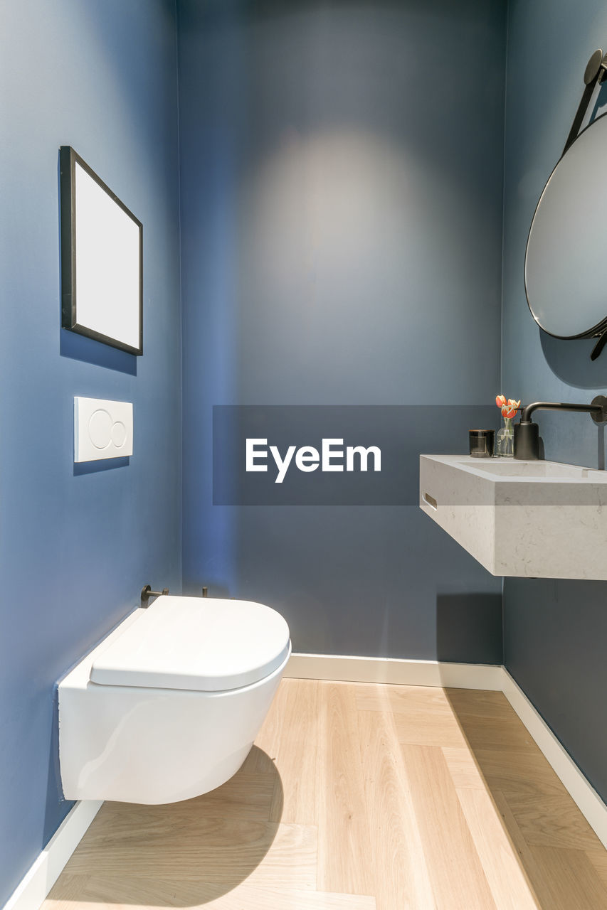 Stylish interior of bathroom with white ceramic sink and wall mounted toilet in minimal style