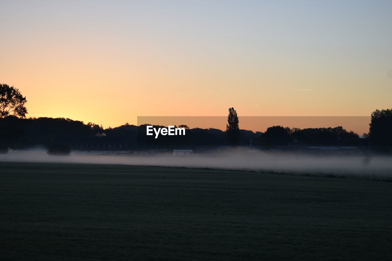 Silhouette trees on field against sky during sunset