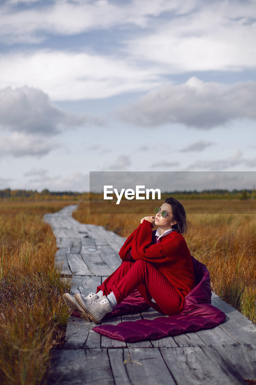 Woman  in red warm clothes and a big scarf on an ecological trail in the autumn not a swamp