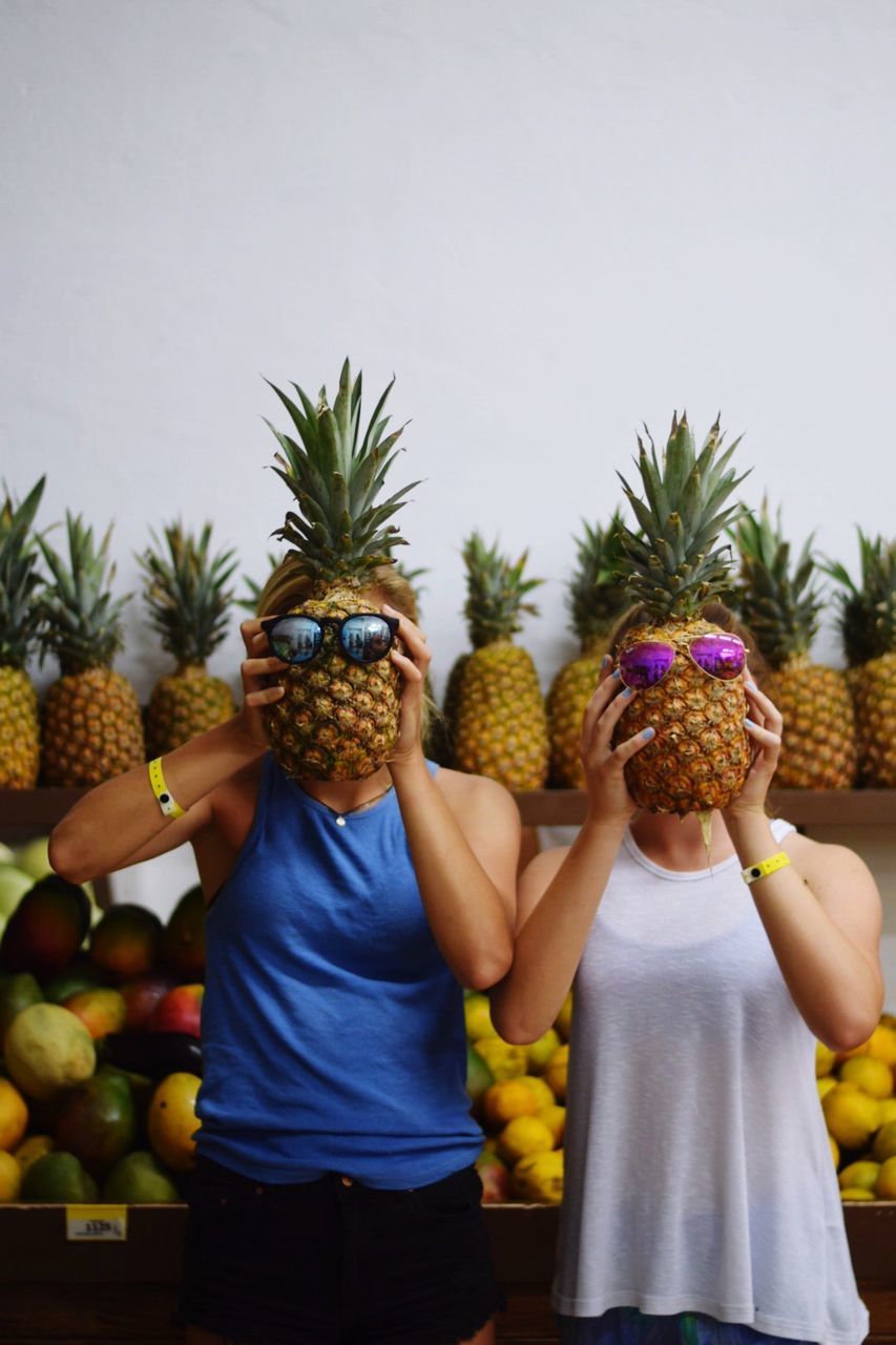 Women covering faces by pineapples