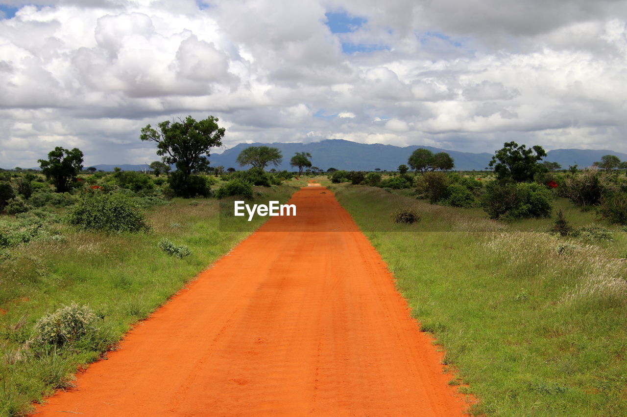 Dirt road amidst field against sky