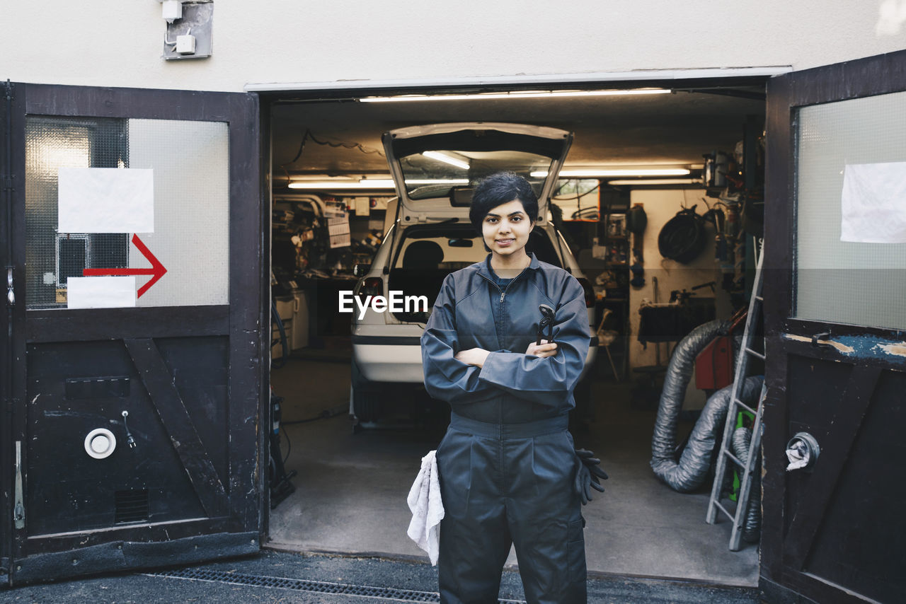 Portrait of confident female mechanic standing at entrance of auto repair shop