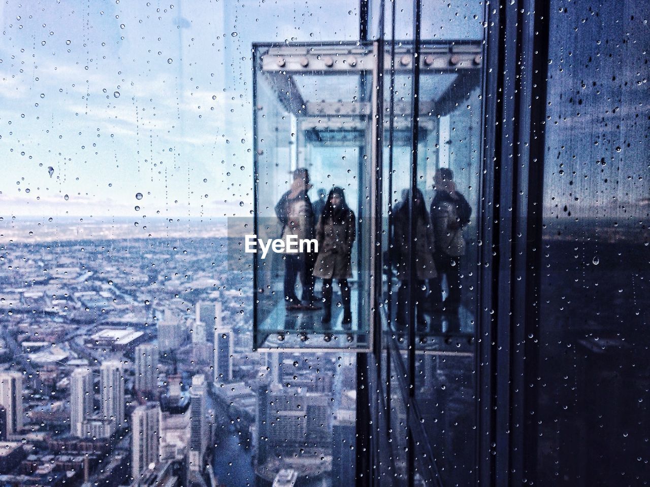 People in glass elevator over cityscape during rainy season
