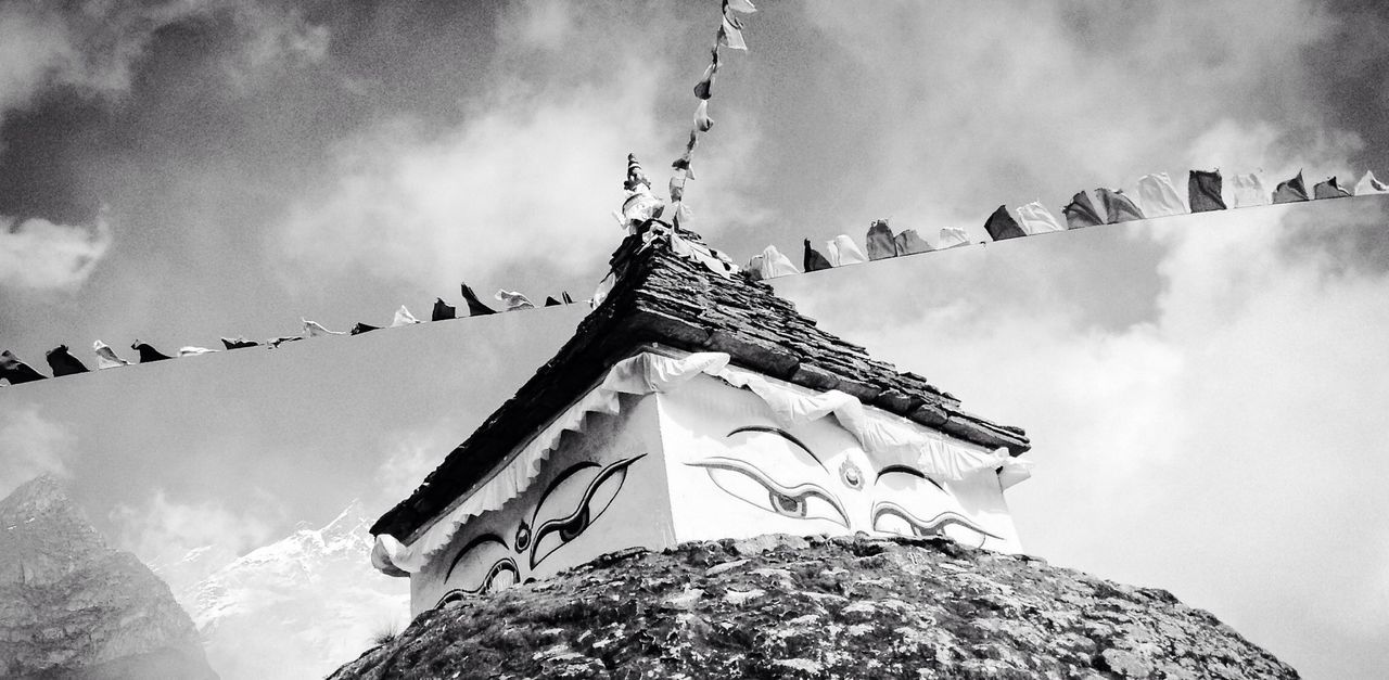 Low angle view of prayer flags and temple against cloudy sky