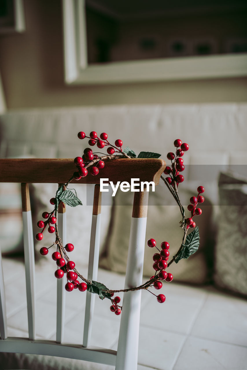 Simple wreath made with decorative red berries placed on chair in cozy room during christmas preparation