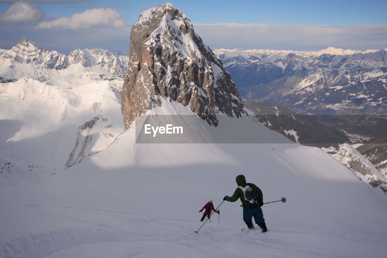 HIGH ANGLE VIEW OF PEOPLE SKIING ON SNOWCAPPED MOUNTAINS