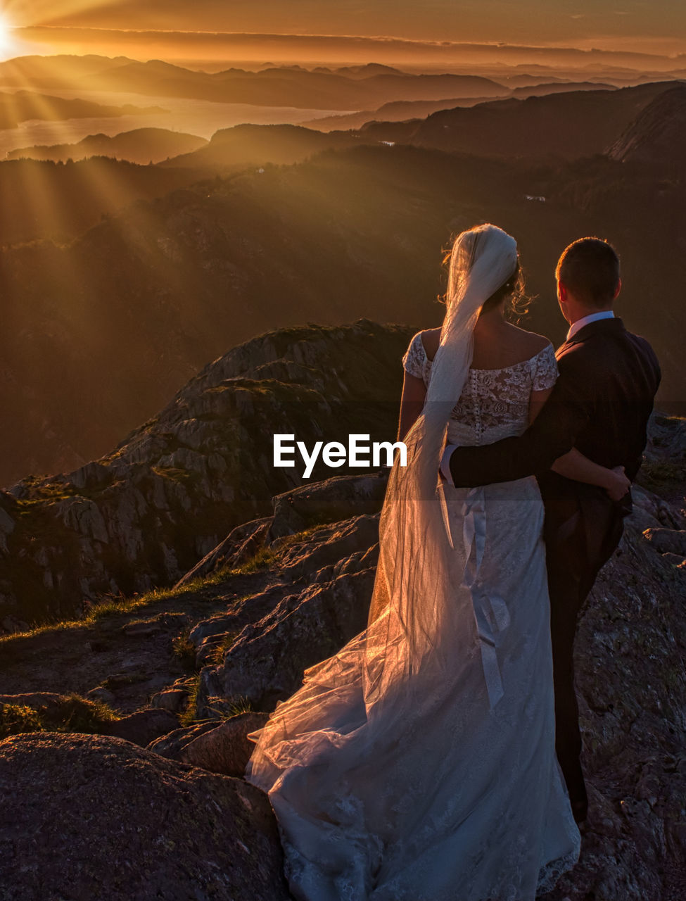 REAR VIEW OF COUPLE ON MOUNTAIN AGAINST SKY