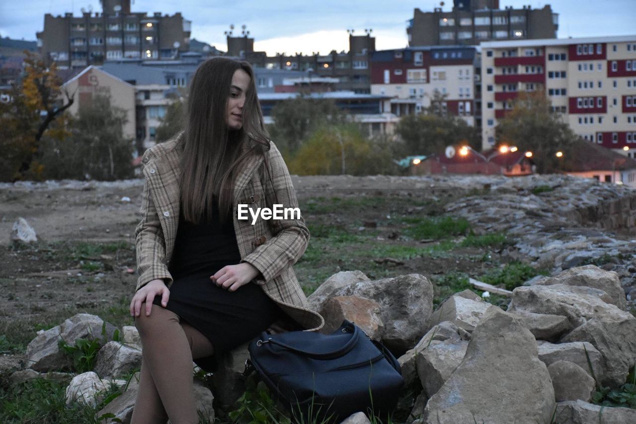 Woman sitting on rock at field in city