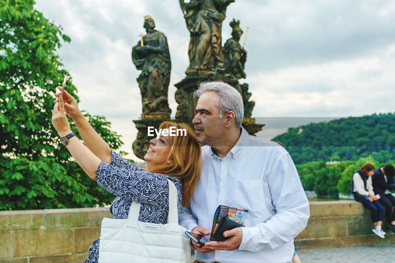 YOUNG MAN PHOTOGRAPHING WOMAN USING SMART PHONE WHILE STANDING ON ROCK