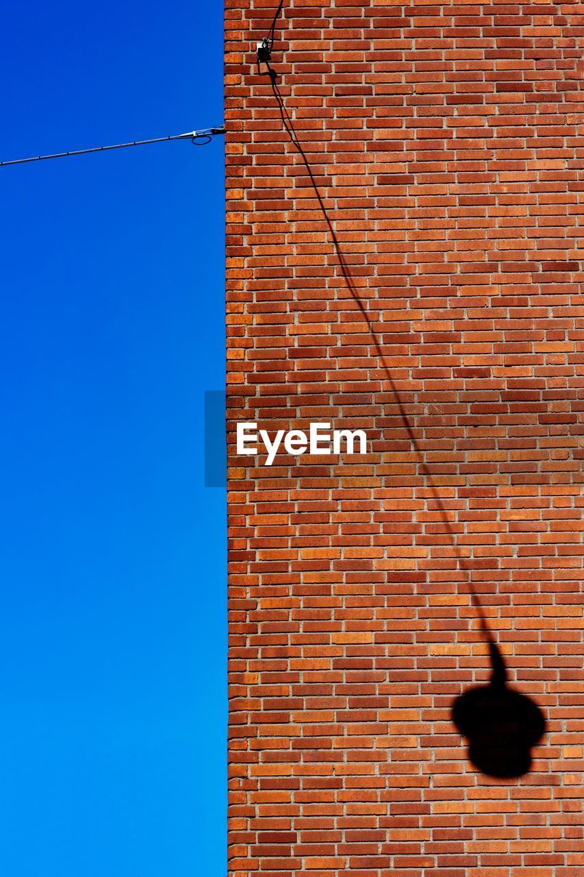 Low angle view of brick with a lamp shadow wall against clear sky