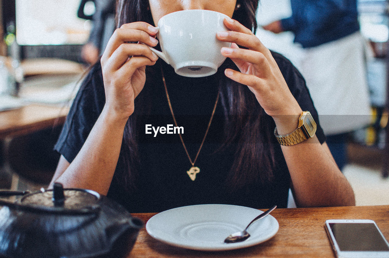 Midsection of woman drinking coffee at table in cafe