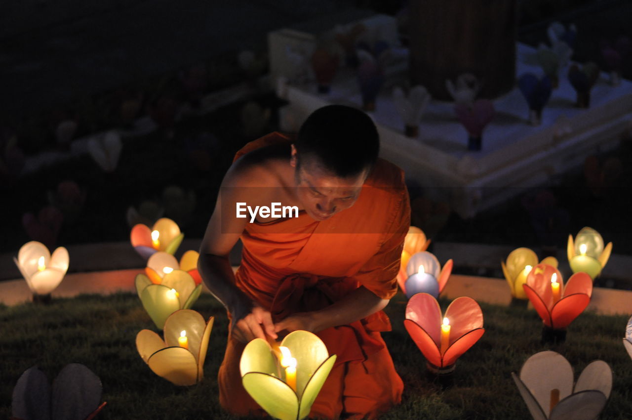 REAR VIEW OF WOMAN SITTING ON ILLUMINATED LIT CANDLES