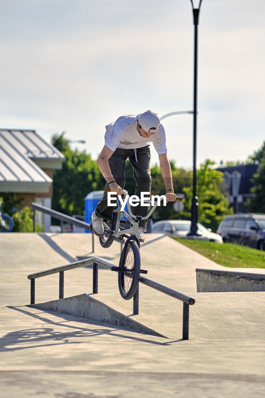 Rider riding bmx bike on railing against sky at skateboard park during sunny day