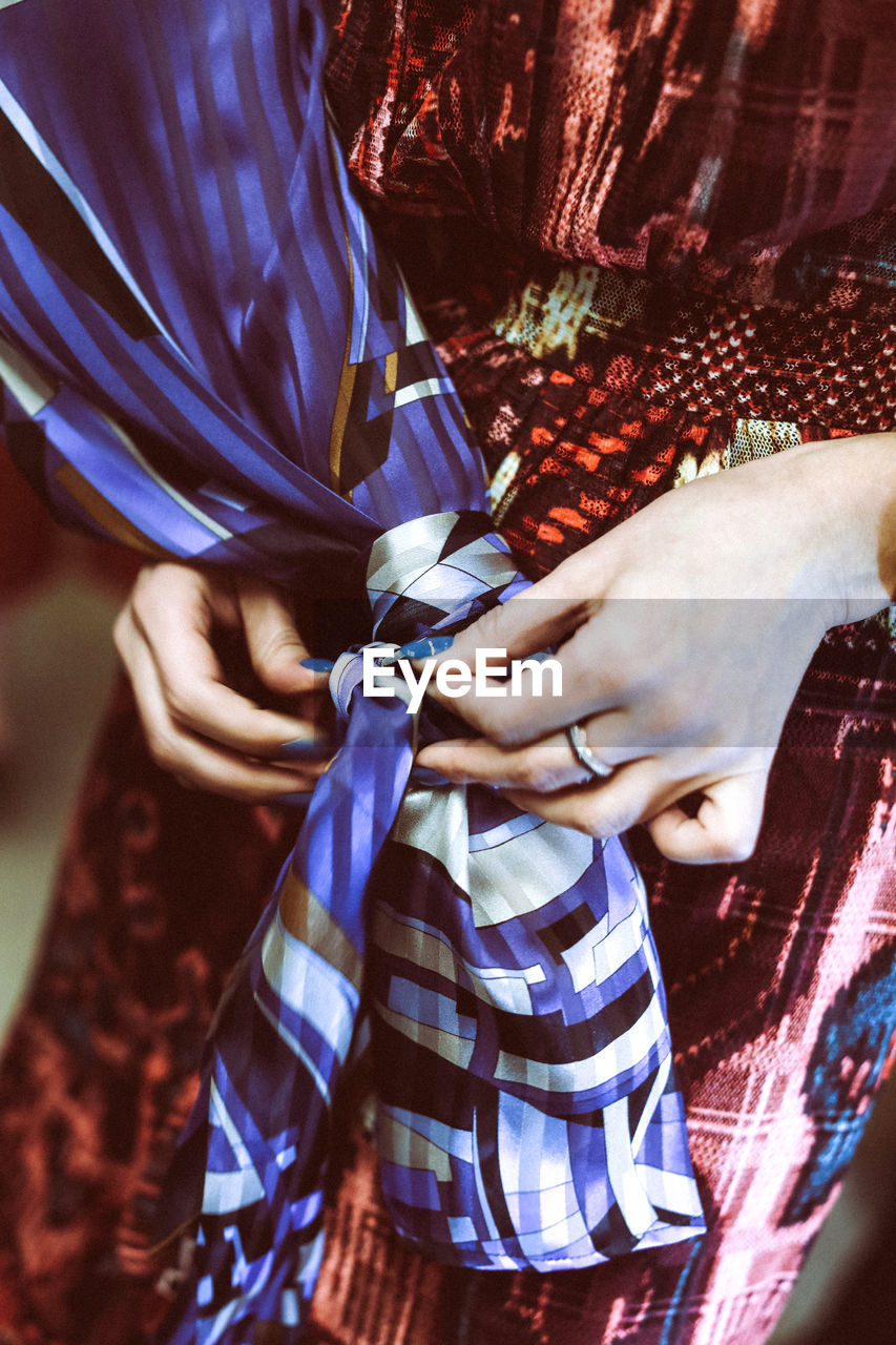 Woman's hand tying silk blue fabric on dress