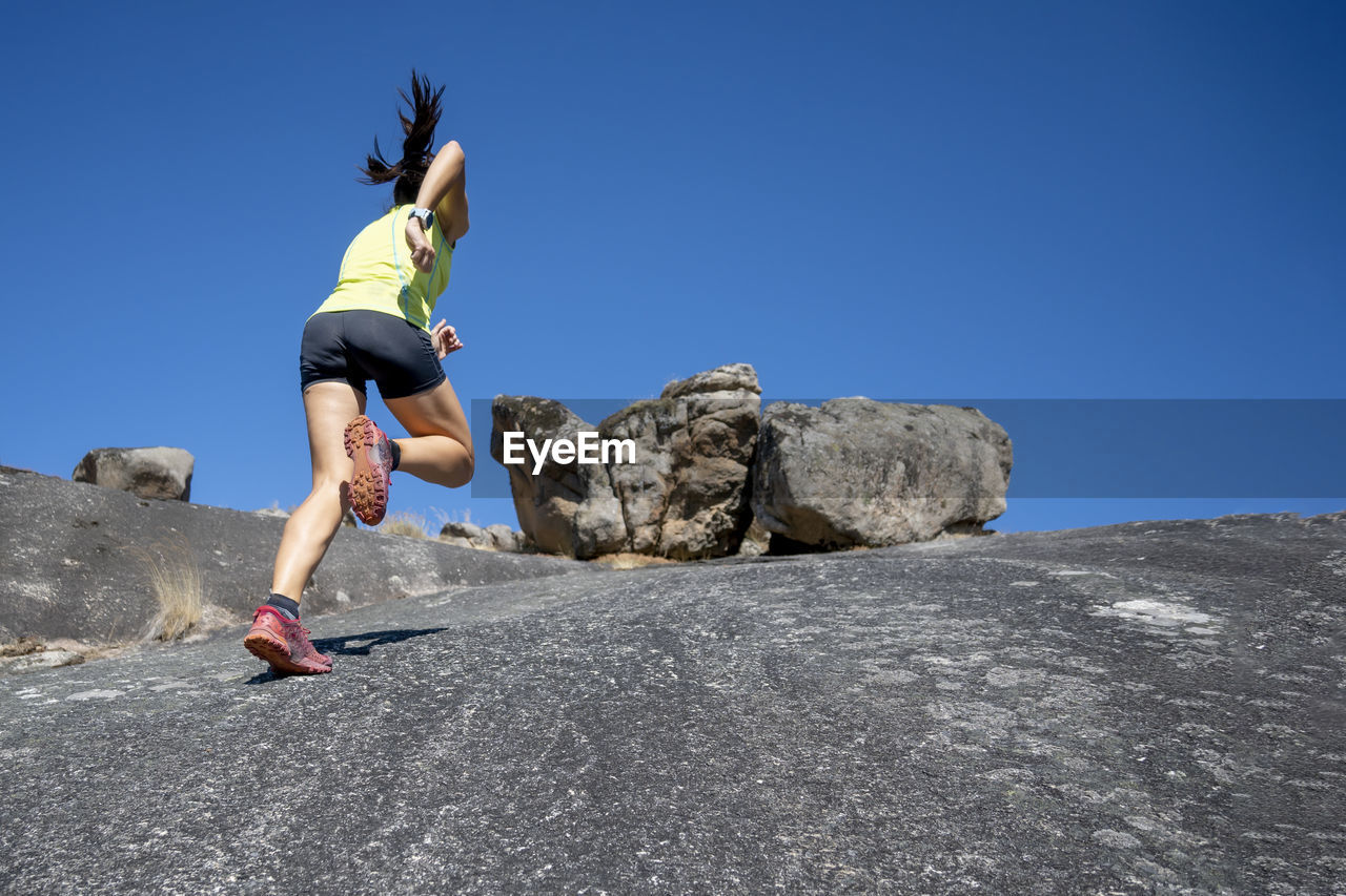 Female athlete running up on rock mountain during sunny day