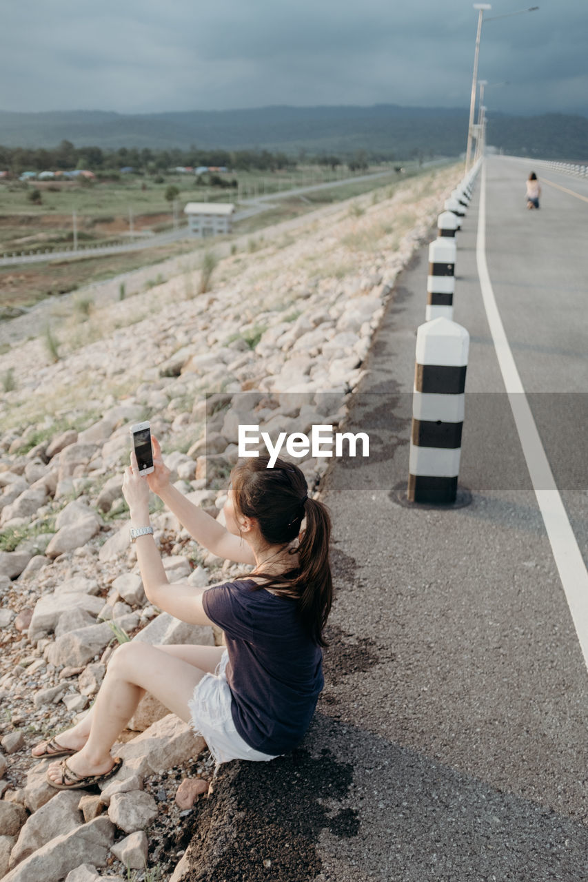 High angle view of woman photographing with smart phone while sitting on road