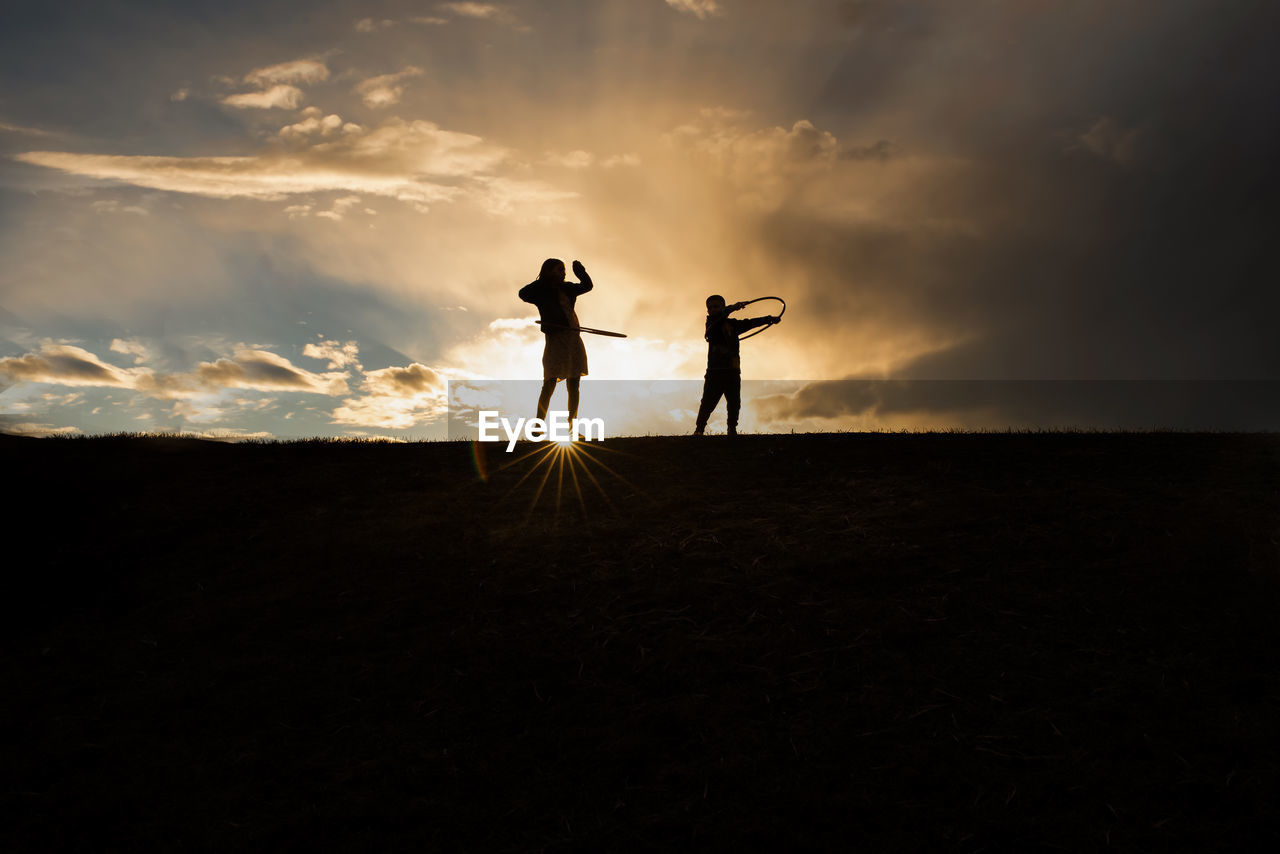 Silhouette of siblings hoola hooping