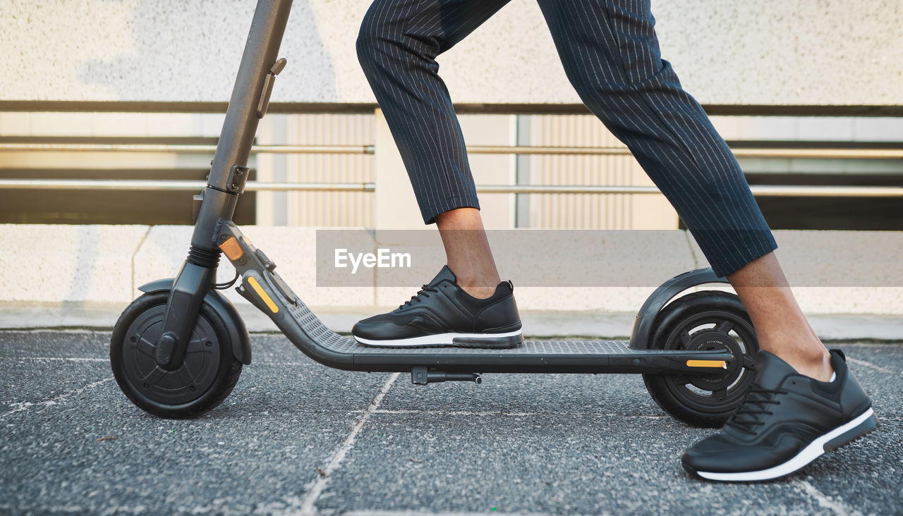 low section of man riding push scooter on field