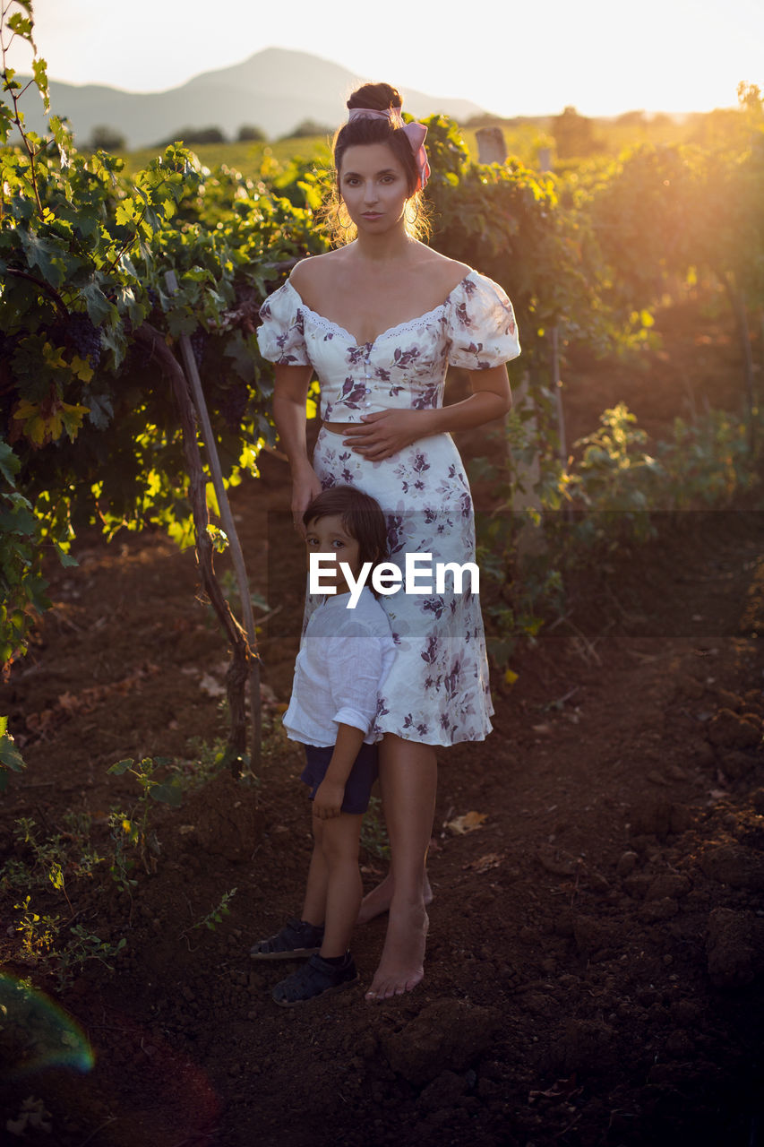 Family mother in a dress with her son walking through a vineyard in summer in italy