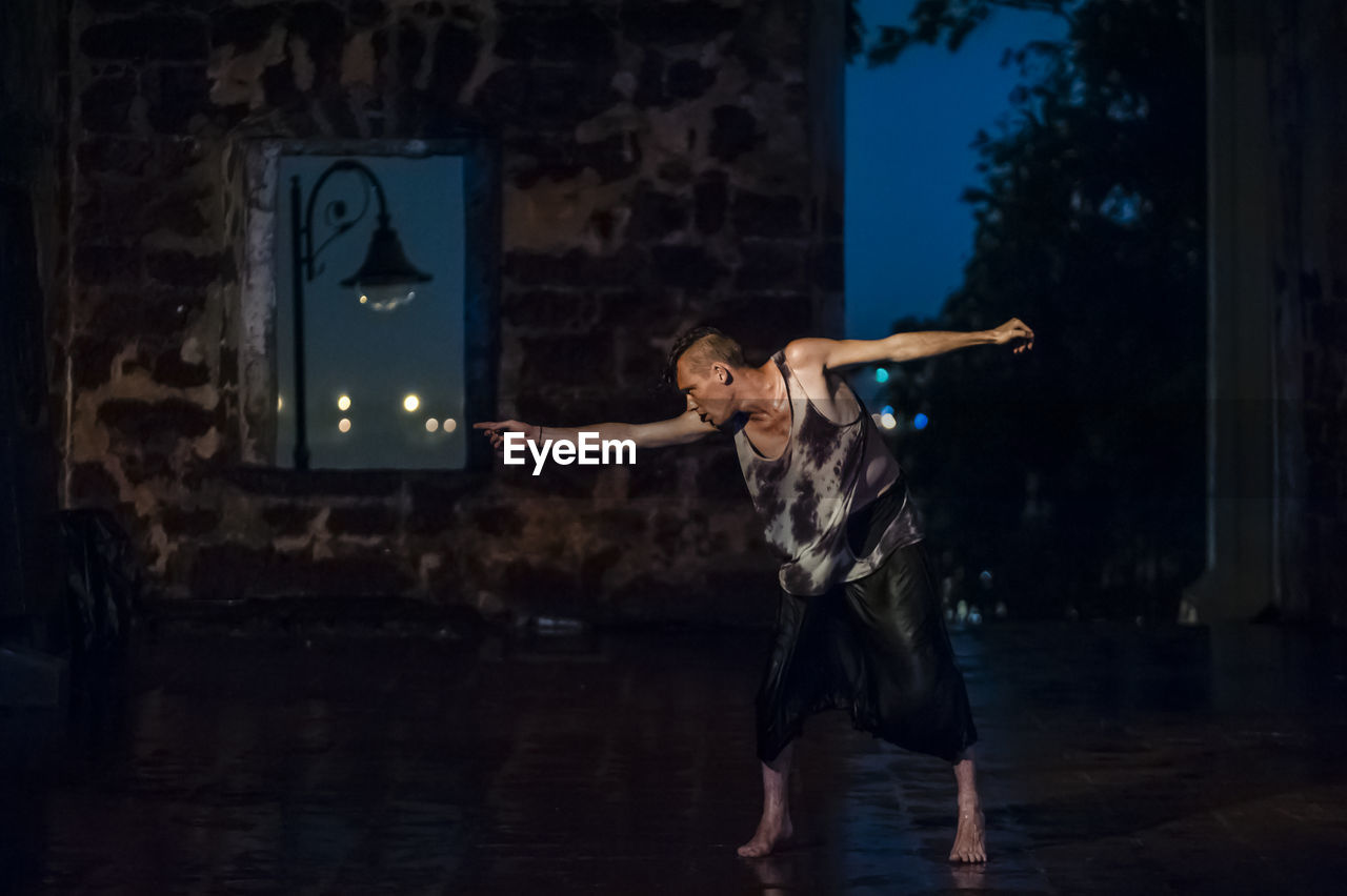 REAR VIEW OF YOUNG WOMAN STANDING AT NIGHT