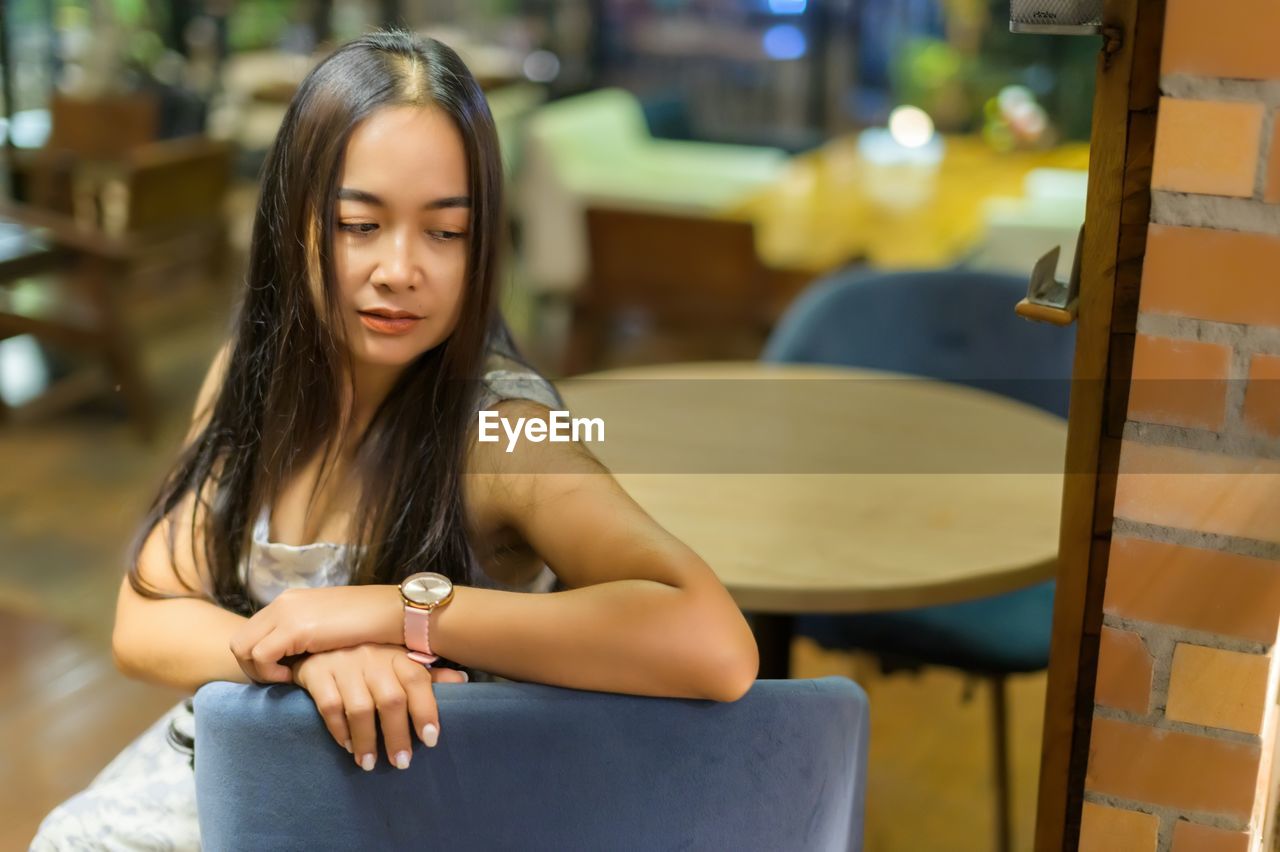 one person, sitting, women, adult, long hair, young adult, hairstyle, emotion, person, casual clothing, lifestyles, teenager, female, brown hair, portrait, furniture, looking, relaxation, clothing, architecture, cafe, chair, photo shoot, focus on foreground, contemplation, child, city, smiling, seat, three quarter length, serious, indoors, front view, happiness, fashion accessory, leisure activity, yellow