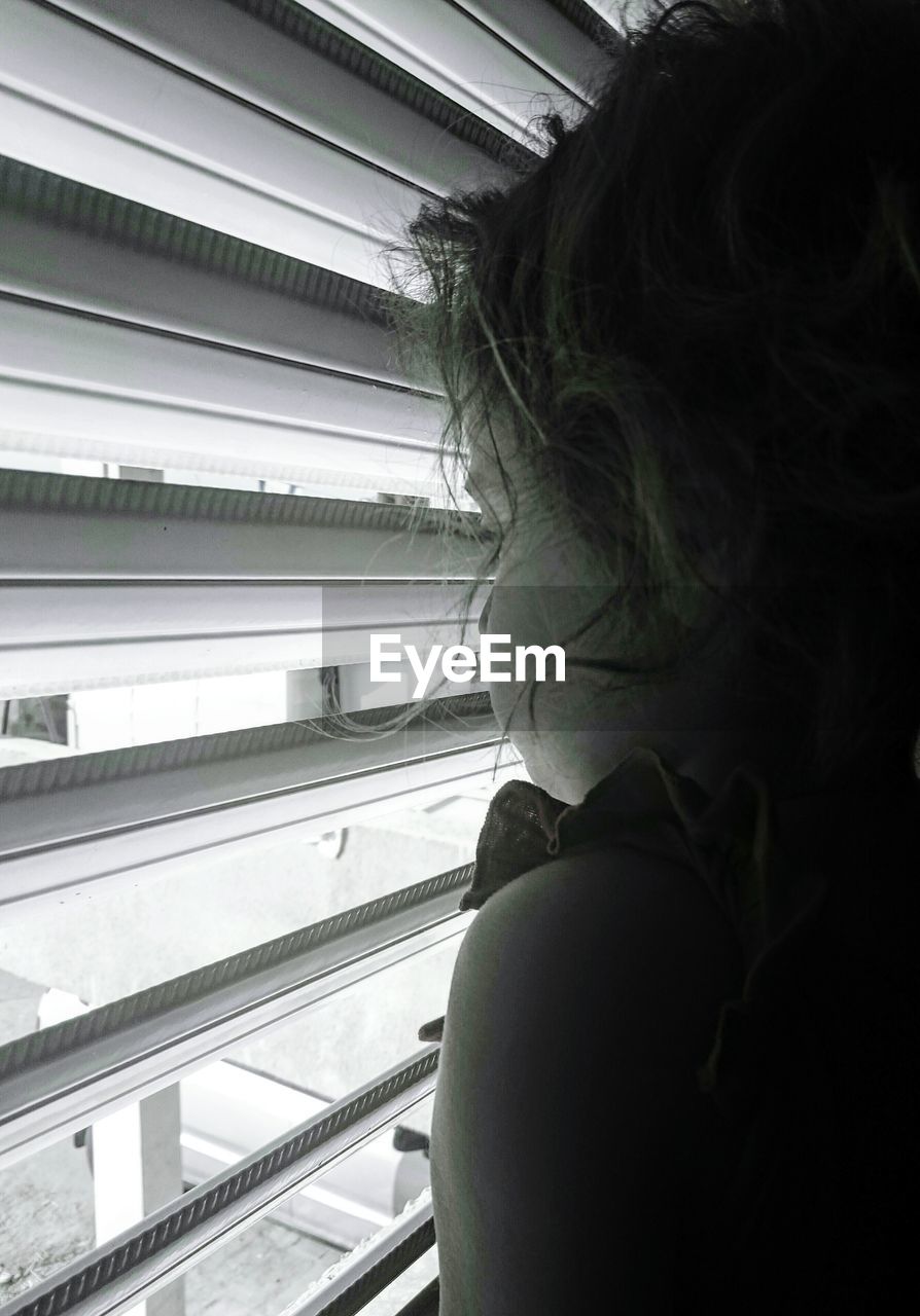 Girl looking through window blinds at home