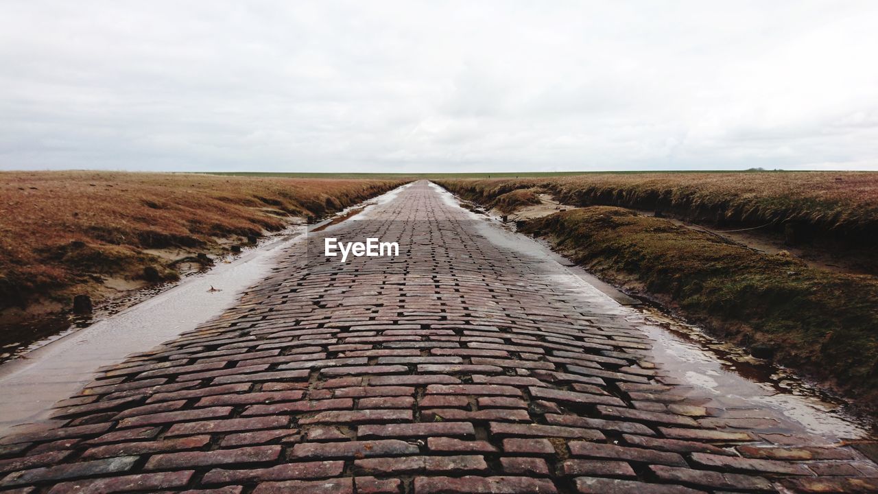 Footpath amidst land against cloudy sky