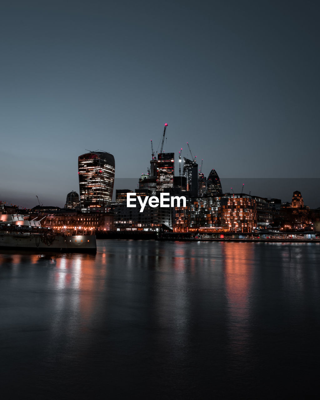 Illuminated buildings by river against sky in city at night