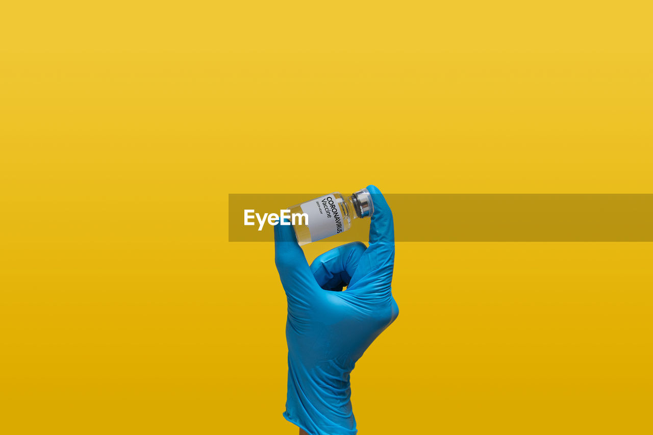 Doctor at laboratory wearing blue rubber glove holding coronavirus vaccine dose bottle label.