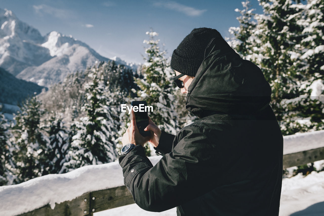 Side view of man photographing with smart phone during winter